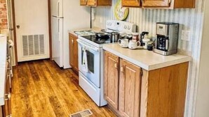 Una cocina compacta con armarios de madera, un refrigerador blanco, una estufa y una cafetera.