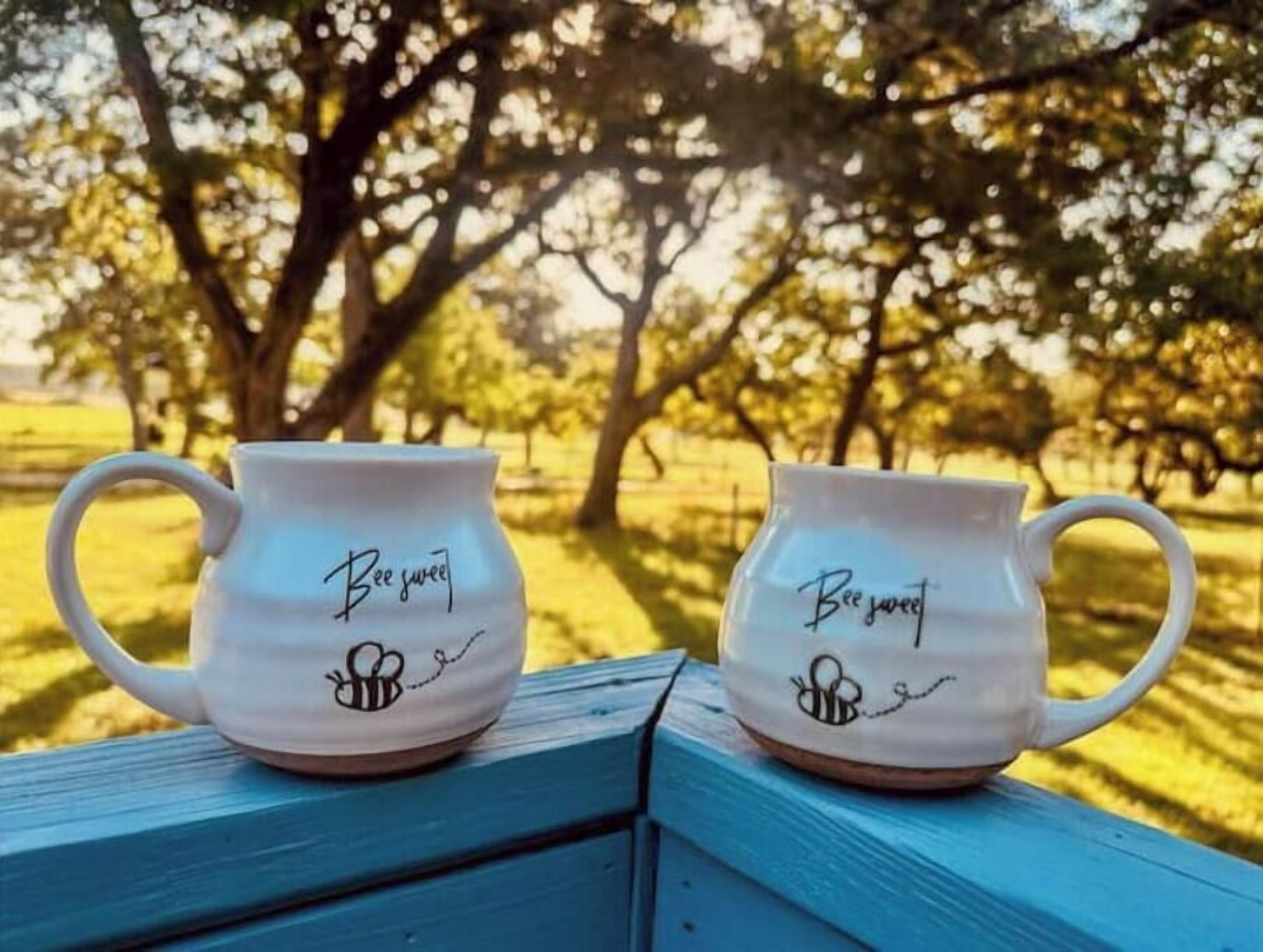 Two white ceramic mugs with "Bee sweet" and a bee logo on a blue wooden surface.