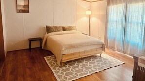 Un dormitorio con cama de madera, mesita de noche, lámpara de pie y ventana con cortinas.