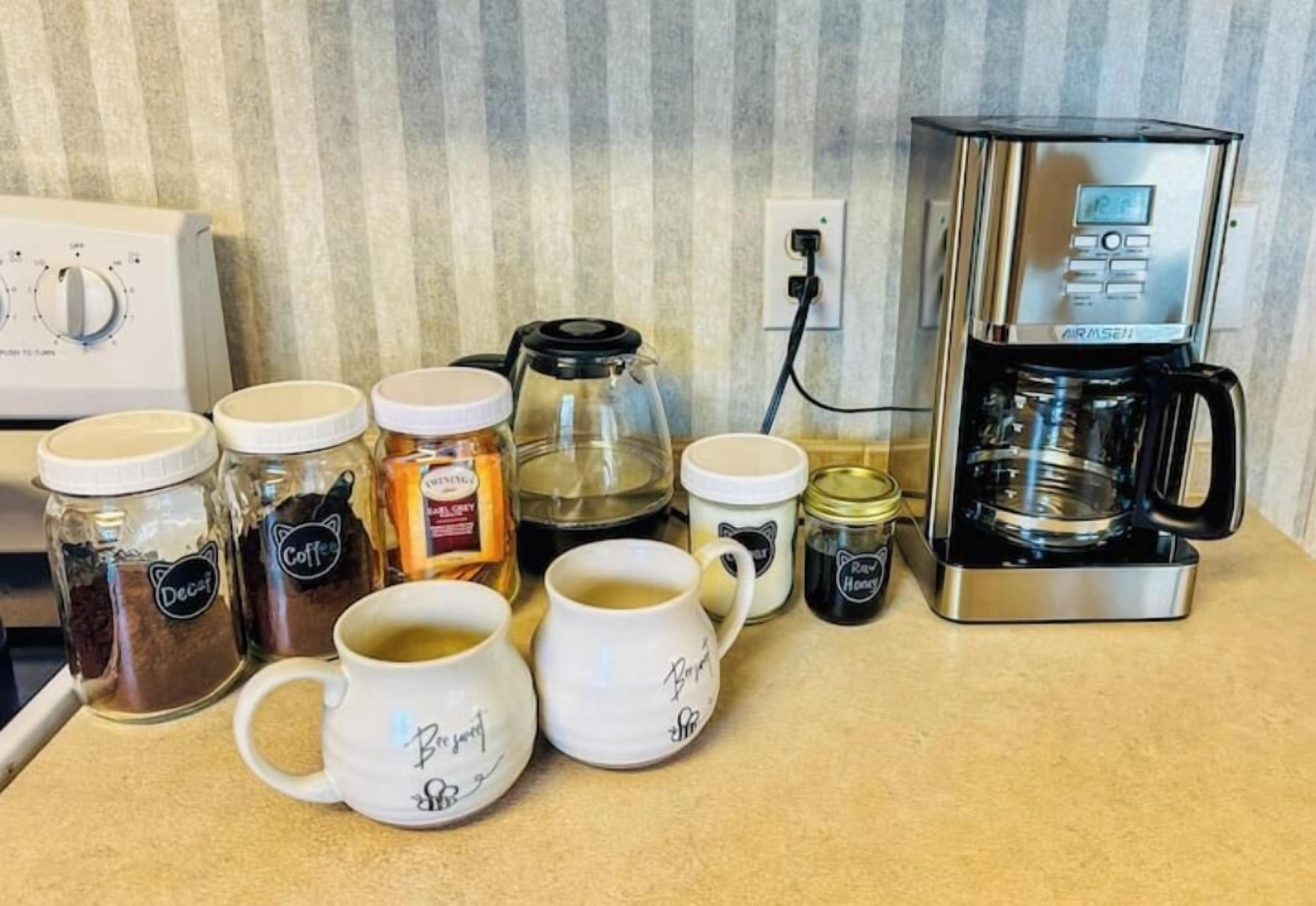 A kitchen counter with coffee-making equipment, including a coffee maker, a glass carafe, and several coffee jars.