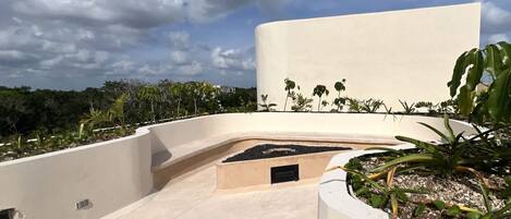 A rooftop terrace with a concrete floor, a small planter with plants, and a white wall.