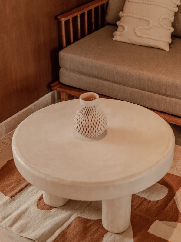 A round white table with a textured vase on top, placed on a patterned rug.