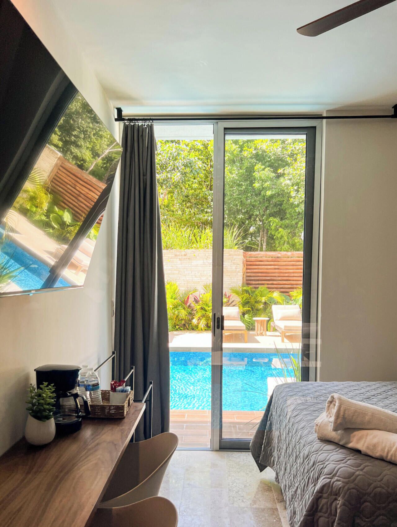 A modern bedroom with a bed, a desk, and a view of a swimming pool.