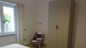 Un dormitorio con cama, una silla, un armario y una ventana con cortinas.