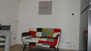 Una sala de estar moderna con un sofá colorido, un cuadro minimalista en la pared y un enchufe visible.