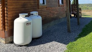 Une cabane en bois avec un balcon, deux réservoirs de propane et une allée gravillonnée.