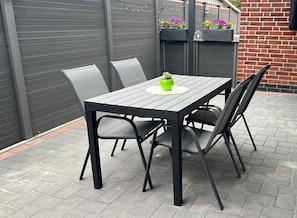 A patio with a table and chairs, a potted plant, and a brick wall. - Barrier-free vacation apartment with covered sun terrace, wallbox, rental bikes  (Krummhörn)