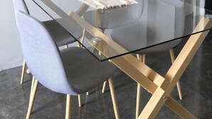 Un'area pranzo moderna con tavolo in vetro, sedie nere e grigie, uno specchio con cornice dorata e un vaso con piante essiccate.