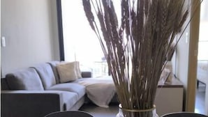 Zona pranzo con tavolo apparecchiato per due persone, un vaso con piante essiccate sul tavolo e un divano sullo sfondo.