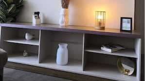 Un soggiorno moderno con una TV a schermo piatto montata sulla parete, un tavolino consolle in legno con ripiani e oggetti decorativi tra cui un vaso con piante secche e un candeliere.