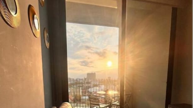 Un soggiorno moderno con un divano, vista sullo skyline urbano attraverso un'ampia finestra, e una zona pranzo visibile attraverso la finestra.