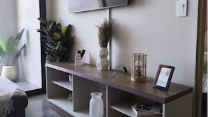 Un soggiorno moderno con una televisione a schermo piatto montata al muro, un tavolino consolle in legno con oggetti decorativi, una pianta in vaso e un divano.