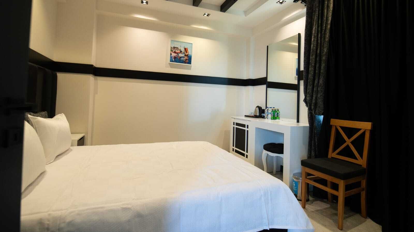 A hotel room with a bed, a desk, a chair, a mirror, and a picture on the wall.