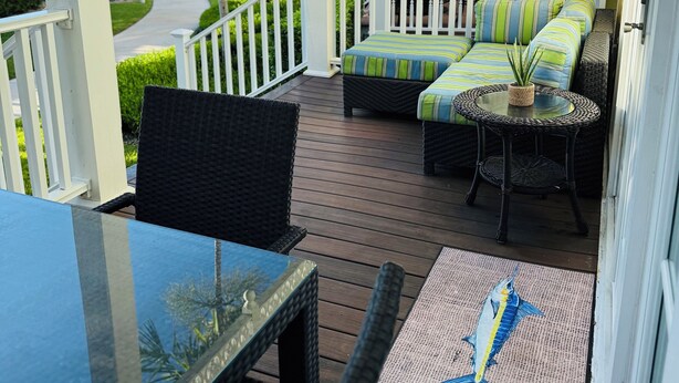 Un espace extérieur aménagé, abrité et doté de meubles en osier et d’une table en verre, offrant une vue sur un jardin bien entretenu et sur l’océan.