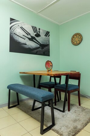 A dining area with a wooden table, blue cushioned chairs, and a bench. A clock and a decorative plate are on the wall.