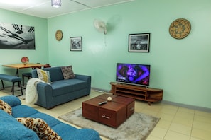 A living room with a blue sofa, a coffee table, a TV, and a wall clock.