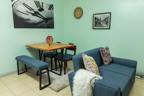 A room with a blue sofa, a wooden dining table with chairs, a bench, and a rug.