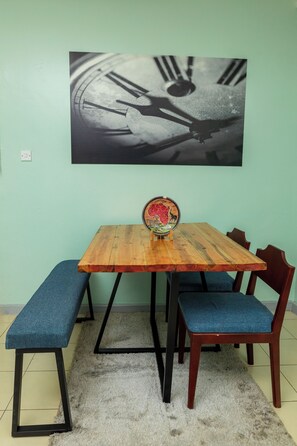 Un comedor con mesa de madera, bancos acolchados azules y un reloj fijado a la pared.