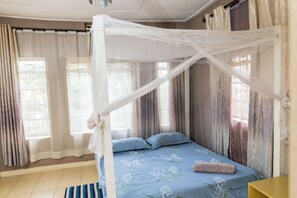 A bedroom with a canopy bed, a bedside table, and curtains on the windows.