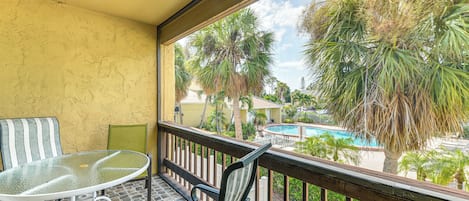 A balcony with a glass table and chairs, overlooking a swimming pool and palm trees.