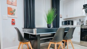 A modern kitchen with a black countertop, white cabinets, and a microwave. There is a potted plant on the countertop and a fire alarm on the wall.