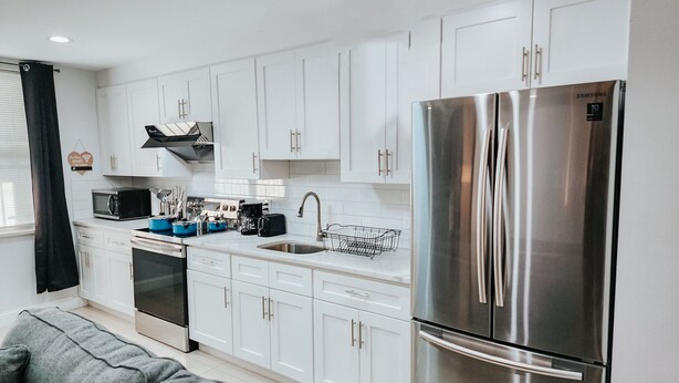 A modern kitchen with white cabinets, a stainless steel refrigerator, a microwave, and a stove.