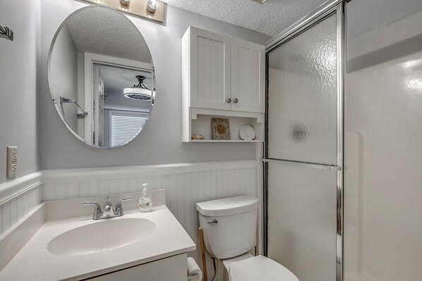 A bathroom with a white sink, mirror, toilet, and shower. - Oceanfront Corner Condo 2BR (North Myrtle Beach)