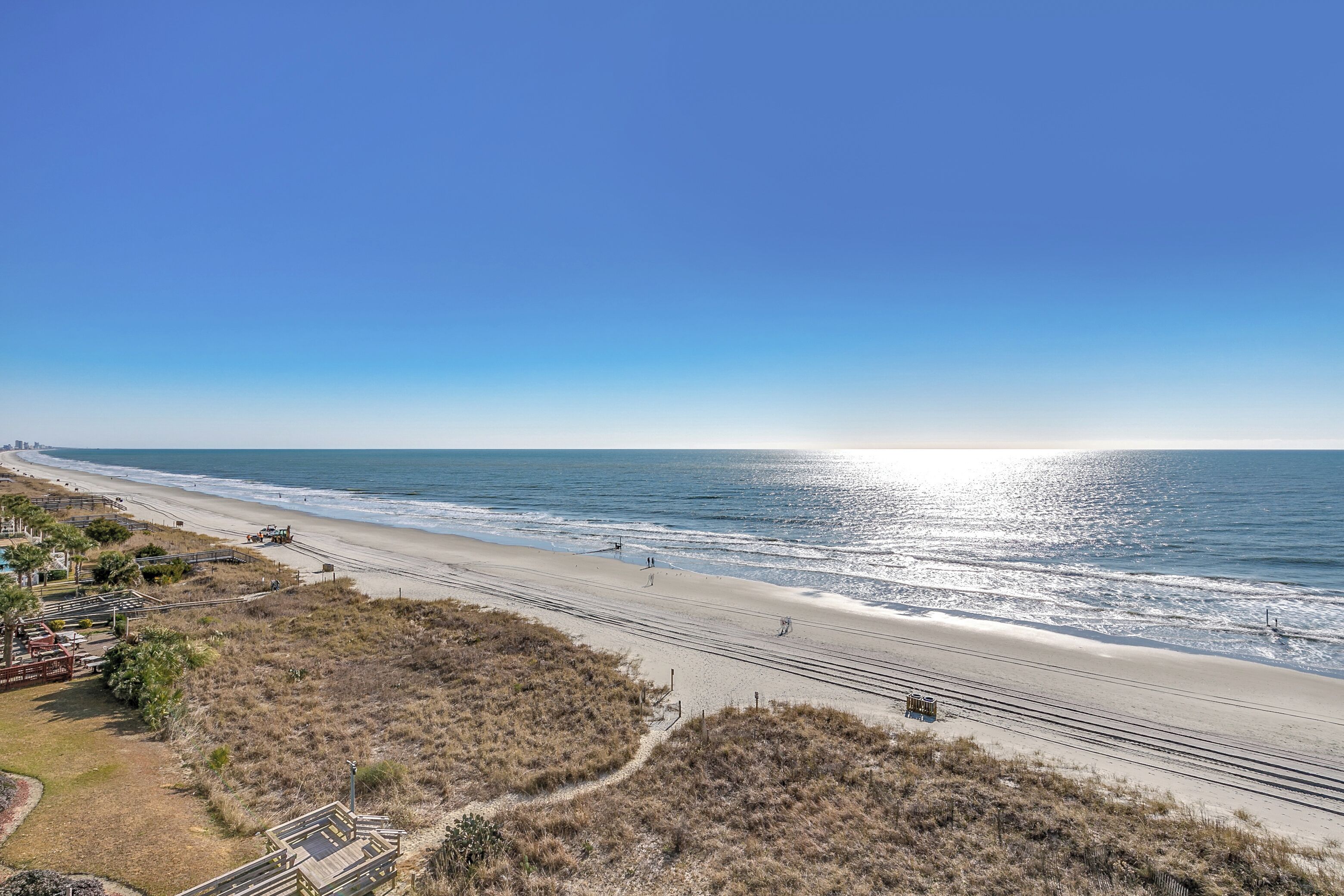 Een strand met een heldere lucht, zandstrand en enkele mensen die wandelen.
