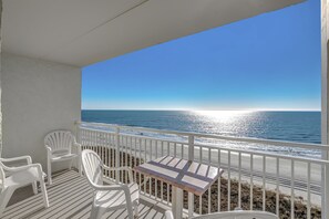 Un balcón con sillas y mesa blancas, con vista a una playa, el océano y un cielo despejado.