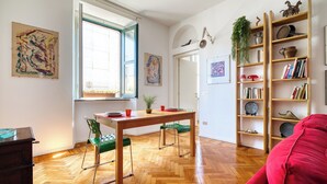 A room with a wooden herringbone floor, a dining table with chairs, a bookshelf, and a red sofa. - San Vincenzo - Milano Centro Storico (Milano)