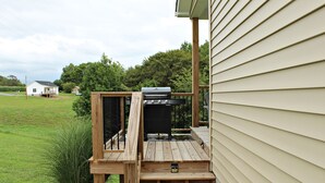 Une terrasse en bois avec un barbecue, une petite table et un marchepied menant à une maison.