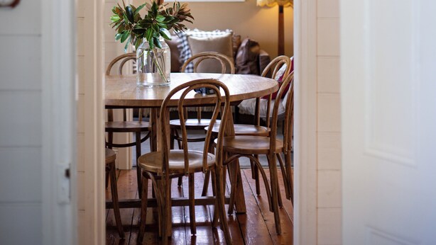 Un coin repas avec une table et des chaises en bois, un vase avec des plantes et un luminaire suspendu.