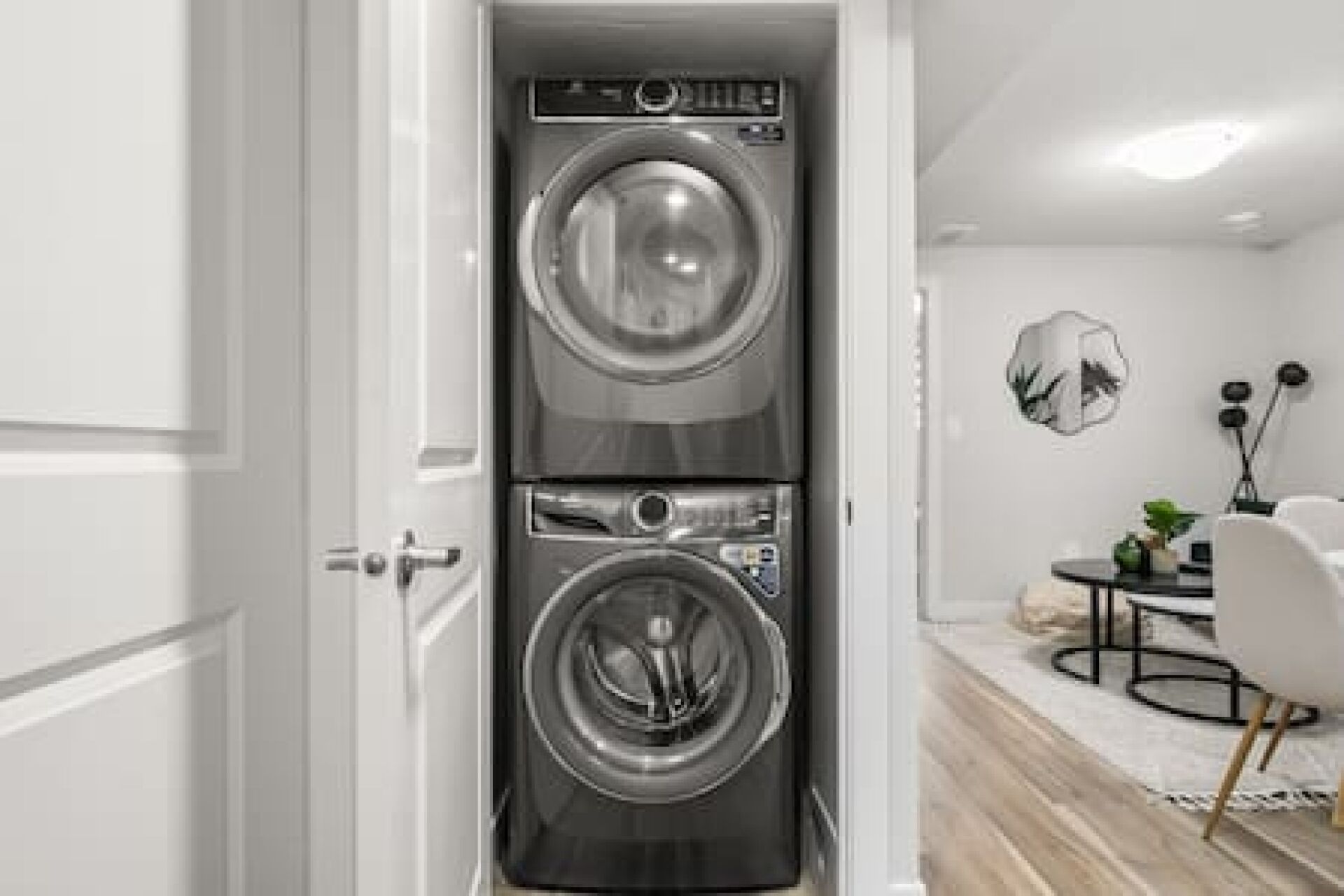 A compact, modern laundry room with a front-loading washer and dryer, a small table with a plant, and a wall-mounted light fixture.