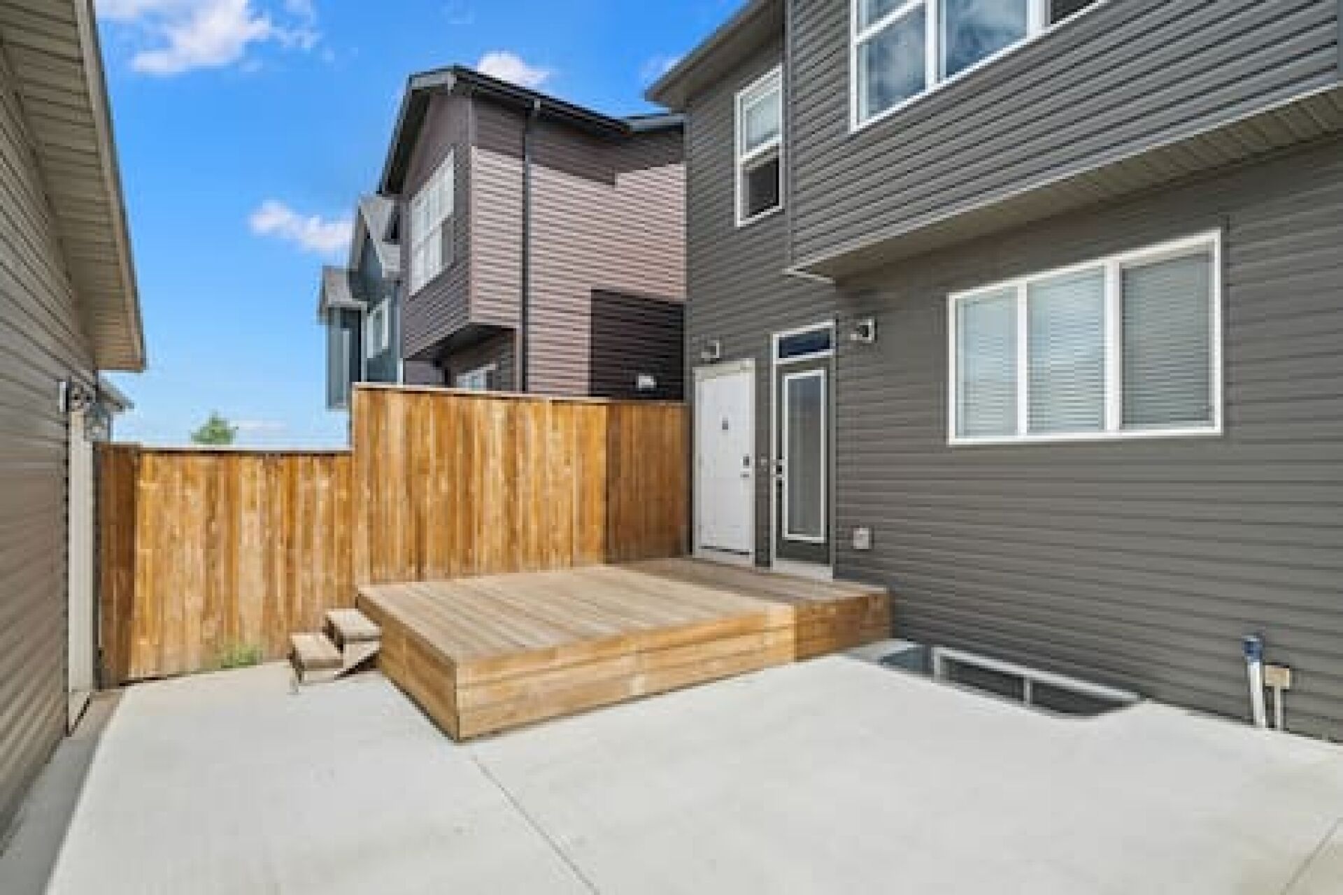 A residential building with a wooden deck, a grey exterior, and a white door.