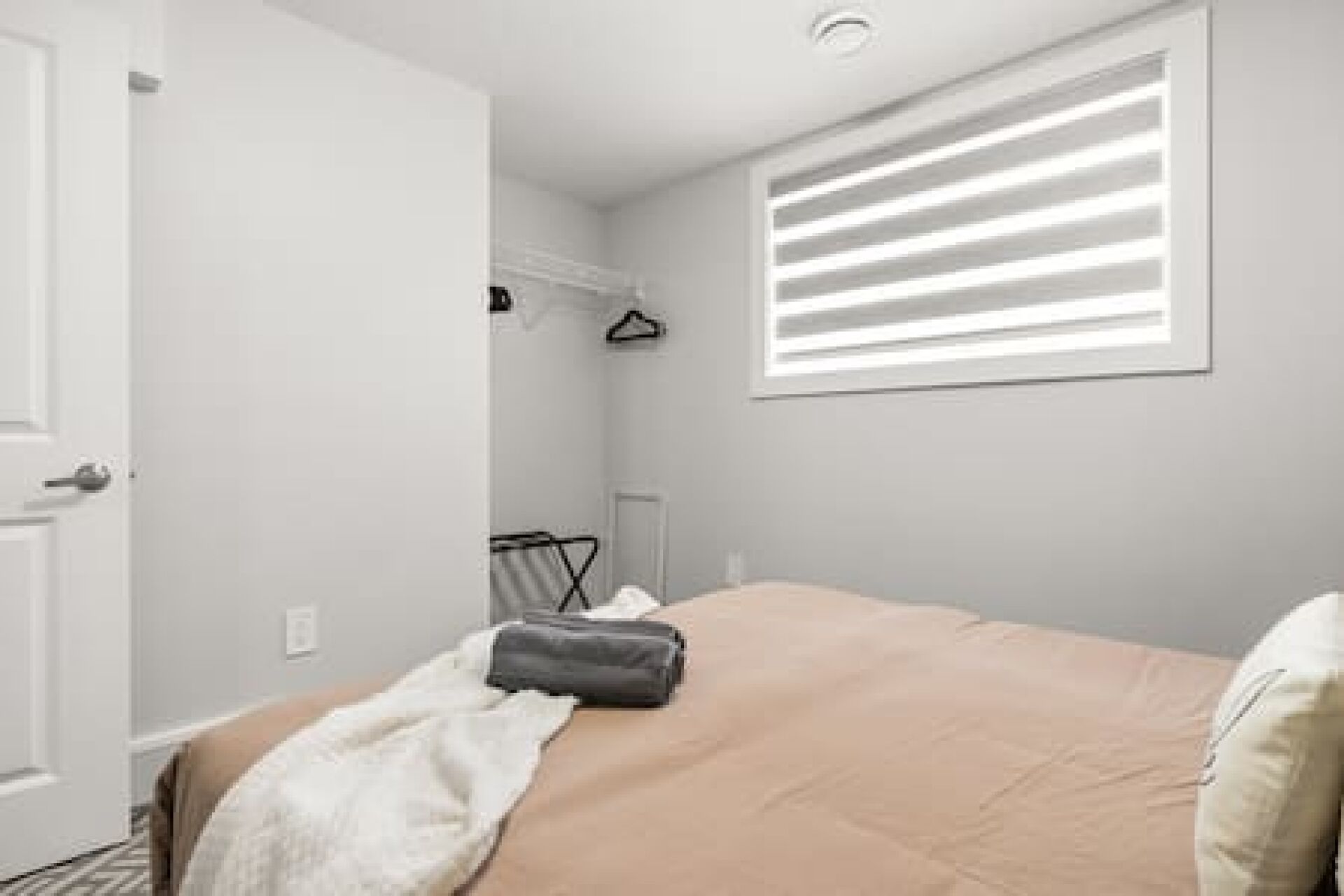 Un dormitorio con cama, ventana con persianas, una puerta y un perchero.