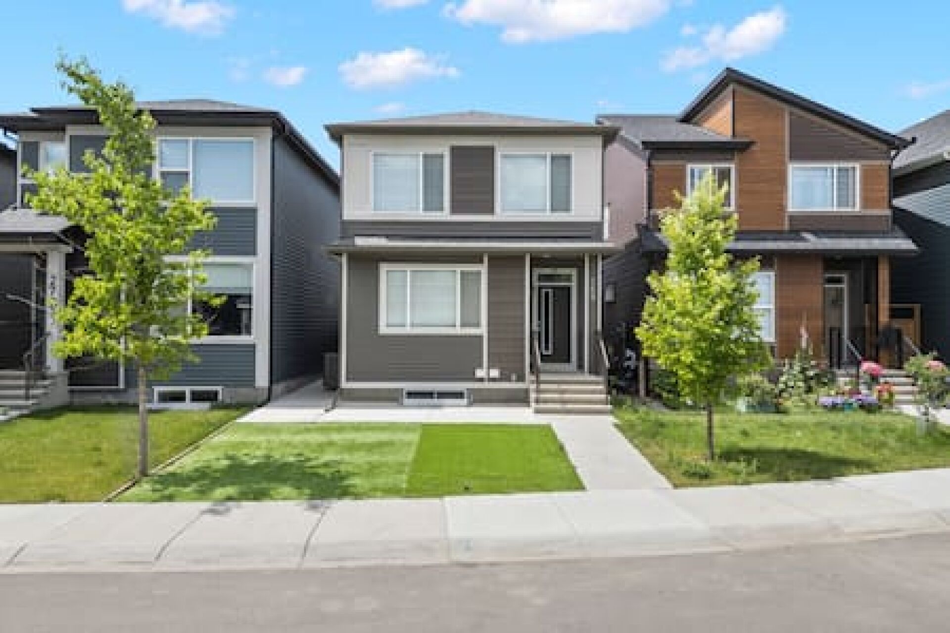 A row of modern townhouses with a central entrance, a small front yard, and a clear sky.
