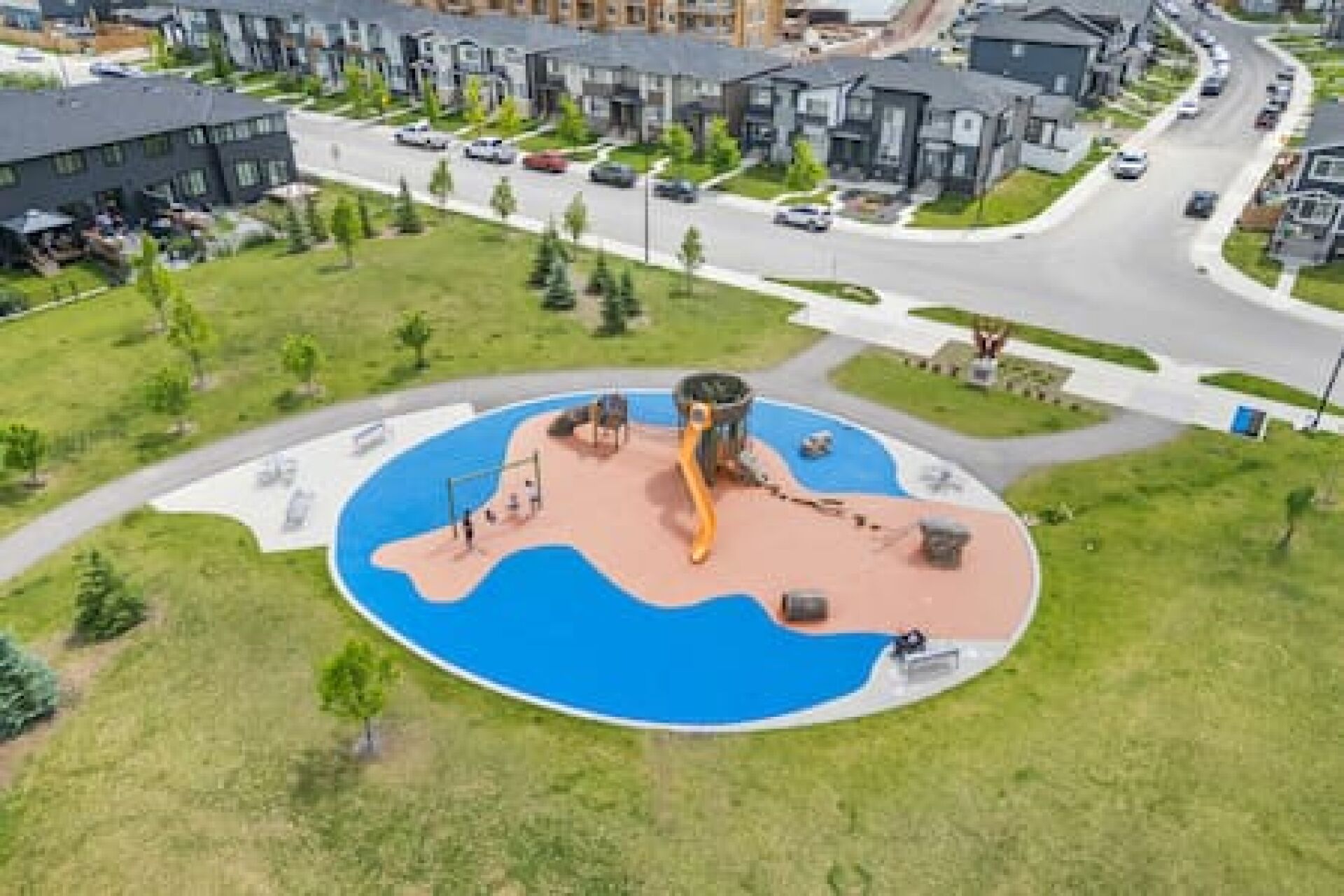 Een woongebied met moderne huizen, een centraal gelegen, rond park met een speeltuin, en een hoofdstraat met auto's.
