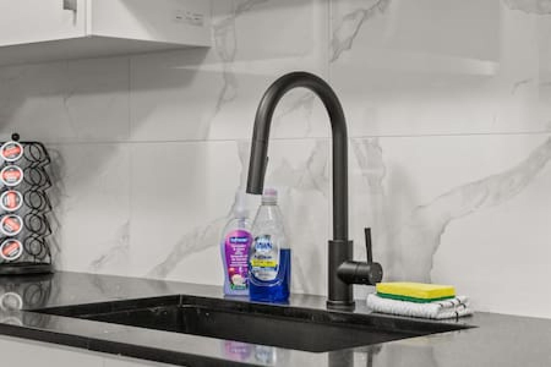 A kitchen with a black faucet, a bottle of dish soap, and a sponge on the counter.