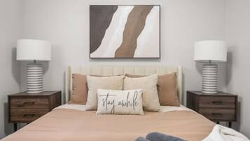 Une chambre à coucher comprenant un lit, deux tables de chevet, une commode, une lampe fixée au mur et un oreiller orné d’un motif.