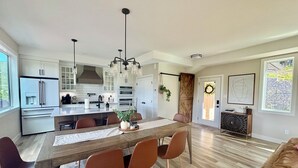Une cuisine moderne avec des meubles blancs, un îlot central et un coin repas comprenant une table en bois et des chaises marron.