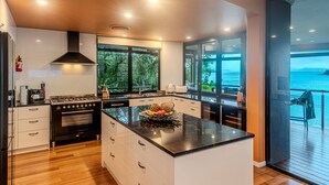 A modern kitchen with a large island, a gas stove, and a view of the sea through large windows. - ABSOLUTE WATERFRONT LUXURY WITH NEW BUGGY (Hamilton Island)