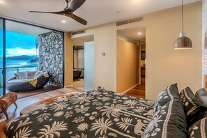 A modern bedroom with a large bed, a view of the sea, a stone wall, and a ceiling fan. - ABSOLUTE WATERFRONT LUXURY WITH NEW BUGGY (Hamilton Island)