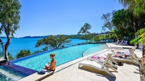 A poolside area with lounge chairs, a pool, and a view of the sea. - ABSOLUTE WATERFRONT LUXURY WITH NEW BUGGY (Hamilton Island)