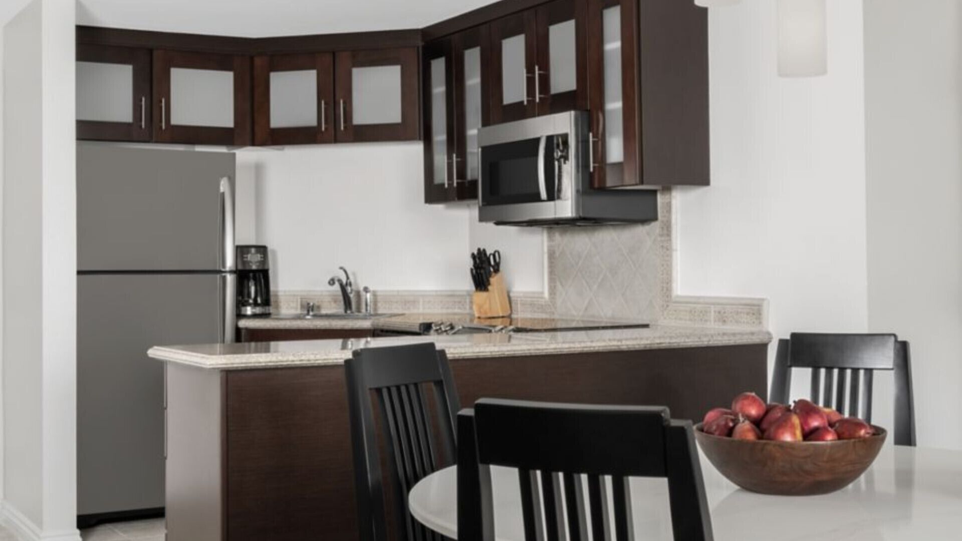 A modern kitchen with dark wood cabinets, stainless steel appliances, and a central island with a bowl of fruit.