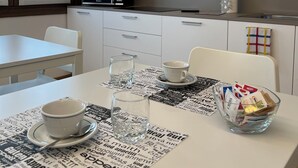 A modern kitchen with a white table, two glasses, a bowl, and a microwave. - Ceciaìs House ROOM 2 (Bassano del Grappa)