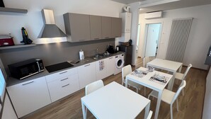 A modern kitchen with a microwave, sink, and washing machine. There are white cabinets and a dining area with a table and chairs. - Ceciaìs House ROOM 2 (Bassano del Grappa)
