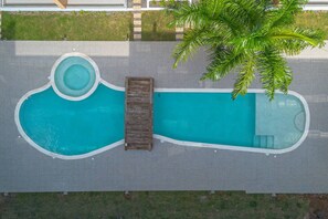 En vy över en swimmingpool sedd ovanifrån, med ett trädäck och en palm.
