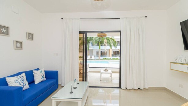 Una sala moderna con un sofá azul, una mesa de centro de vidrio y vista a una piscina y zona de estar exterior a través de un vidrio.