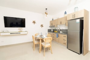 Une cuisine moderne avec des meubles en bois, un réfrigérateur en acier inoxydable, une table à manger avec des chaises et un téléviseur à écran plat fixé au mur.