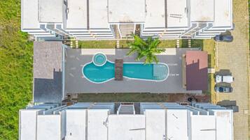 Vista aérea de un edificio moderno con piscina en la azotea, rodeado de espacios para estacionamiento y un pequeño jardín.